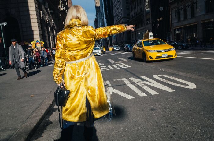 Woman in a yellow coat hailing a taxi on a busy NYC street, capturing the vibrant energy of city life.