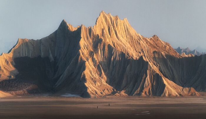 Breathtaking landscape shot of dramatic rugged mountains glowing in warm light under a clear sky, resembling a fantasy movie scene.