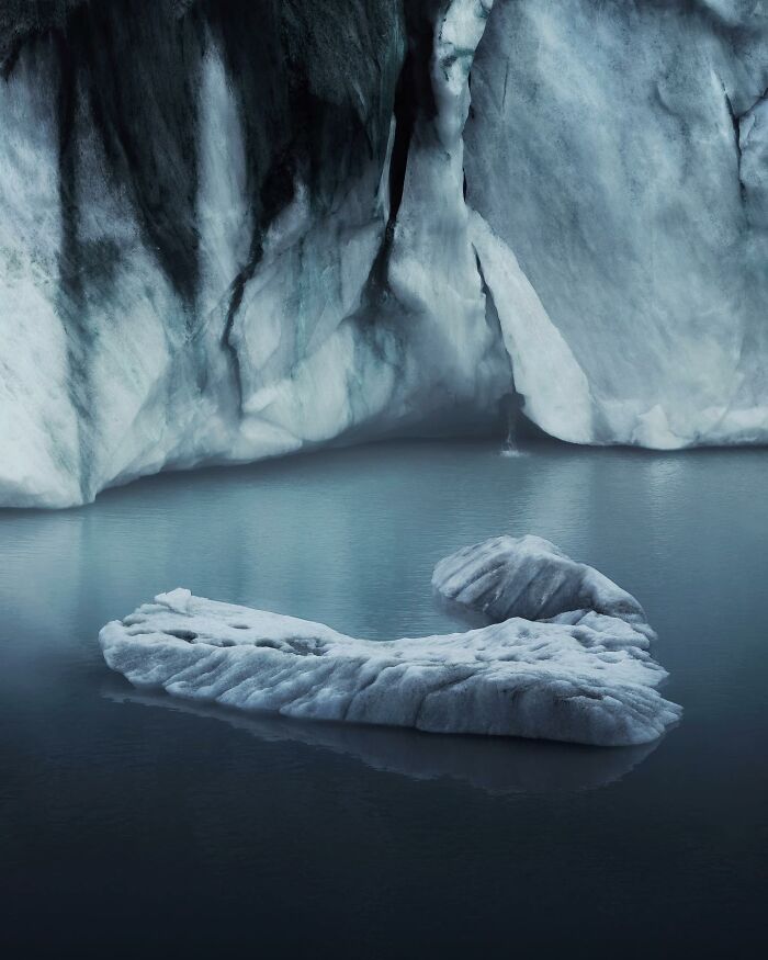 Breathtaking landscape shot of an icy, fantasy-like glacier floating in calm blue waters under rugged cliffs.