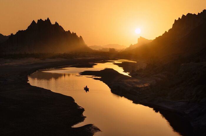 Photographer captures breathtaking landscape shot of a river at sunset with dramatic mountain silhouettes, evoking a fantasy movie scene.