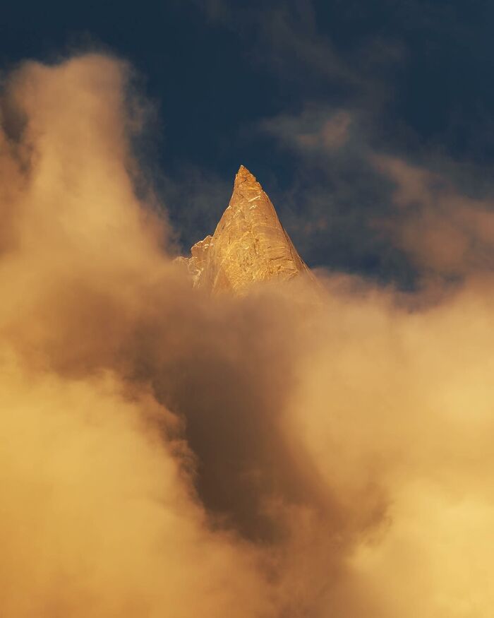 Golden mountain peak emerging through thick clouds in a breathtaking landscape shot resembling a fantasy scene.