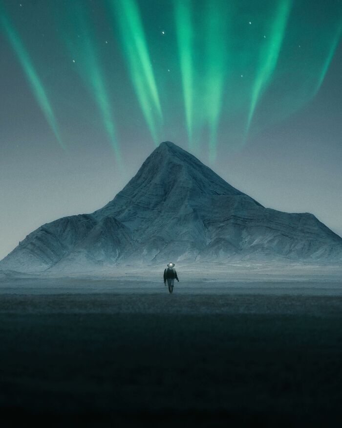 Person walking toward a mountain under breathtaking landscape shots of the northern lights resembling a fantasy movie scene.
