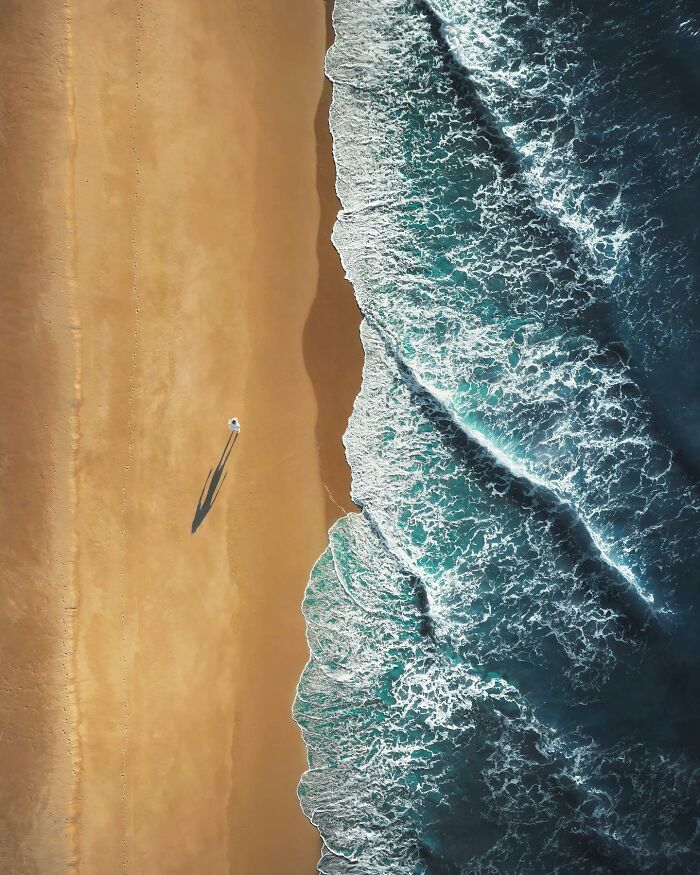 Aerial view of a breathtaking landscape with ocean waves crashing onto a sandy beach, capturing serene natural beauty.