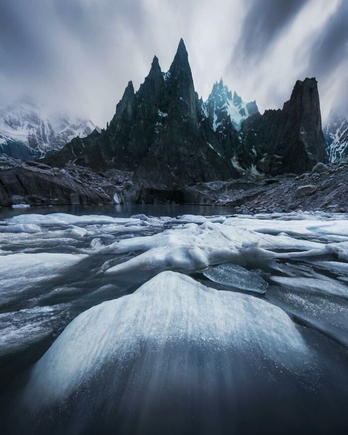 Breathtaking landscape shot of jagged mountains and icy terrain with dramatic clouds, resembling a fantasy movie scene.