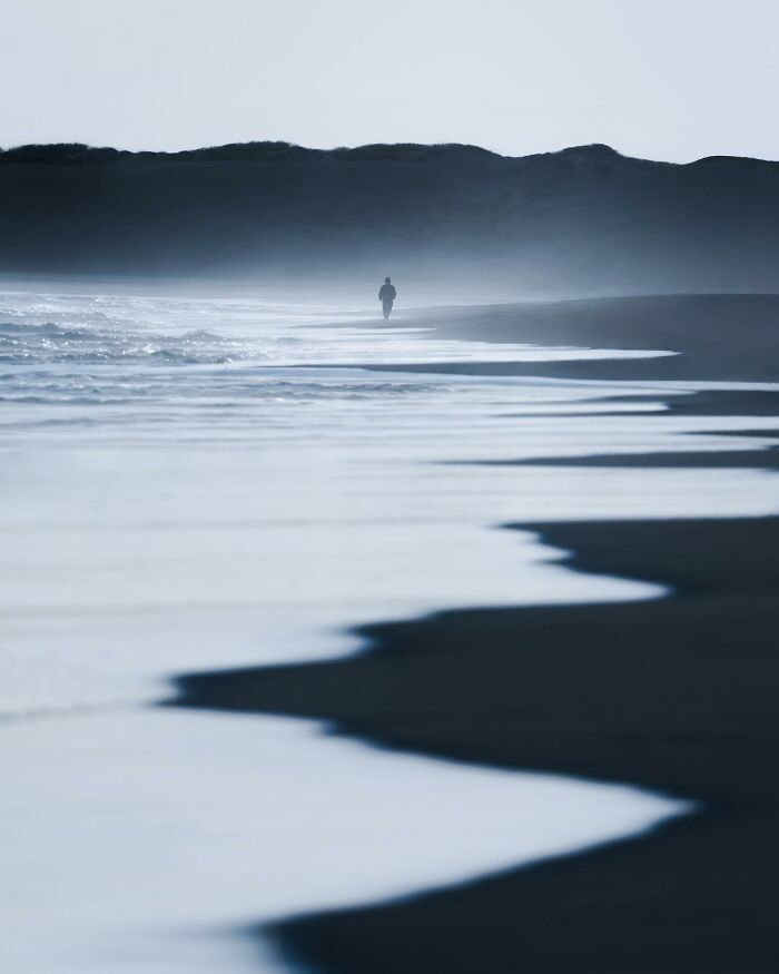 Misty coastline with waves and a lone figure walking, showcasing breathtaking landscape shots resembling a fantasy movie scene.