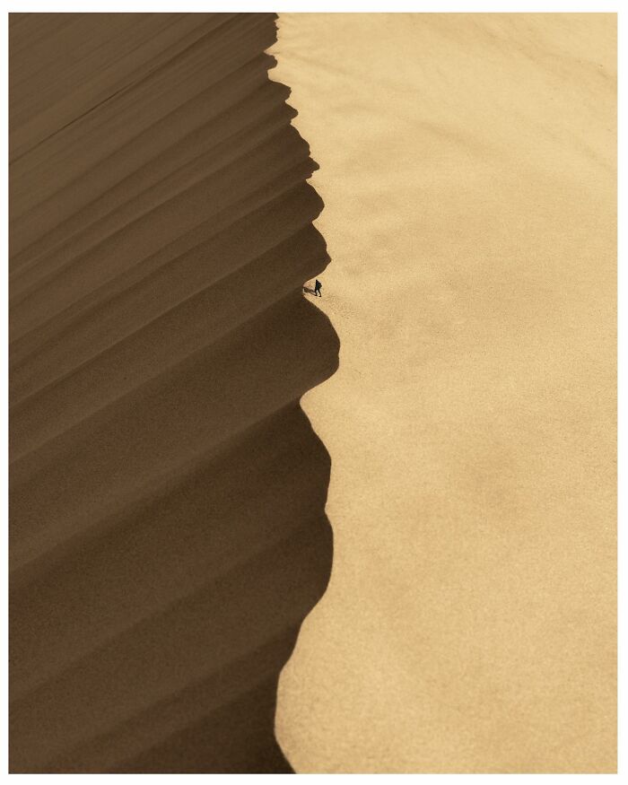 Breathtaking landscape shot of a vast sand dune with sharp contrast and a tiny person climbing its edge.
