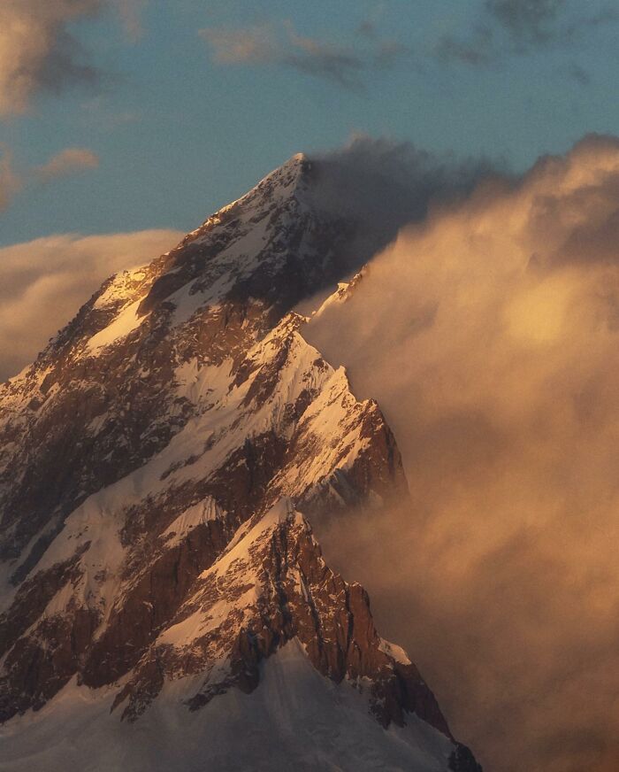 Snow-covered mountain peak partially shrouded in golden clouds during a breathtaking landscape sunset shot.