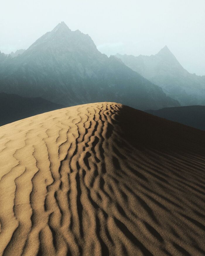 Sand dune with detailed ripples in foreground and misty mountain landscape creating breathtaking fantasy movie-like scene.