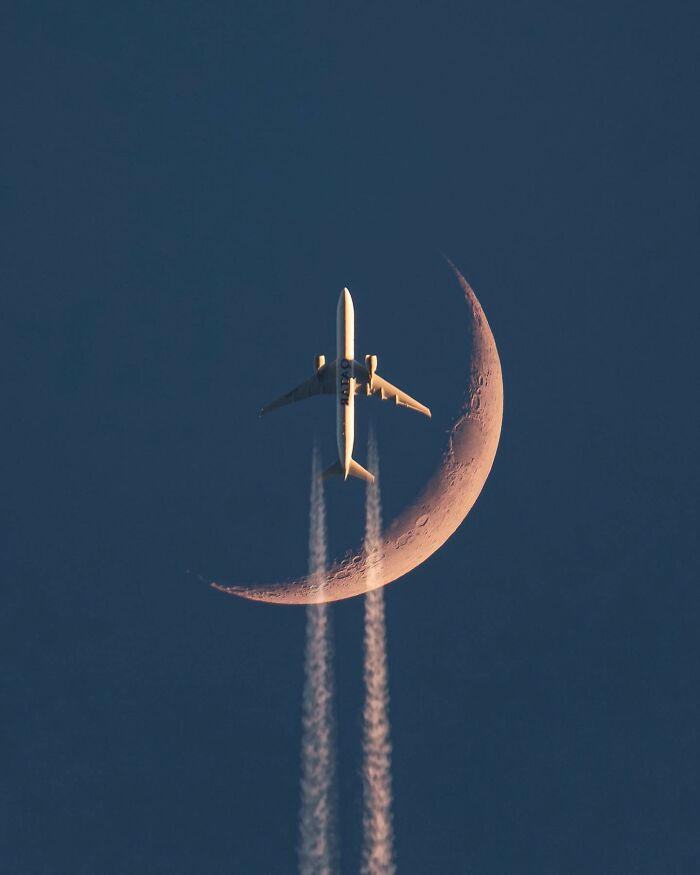 Airplane flying past a crescent moon with contrails, a breathtaking landscape shot resembling a fantasy movie scene.