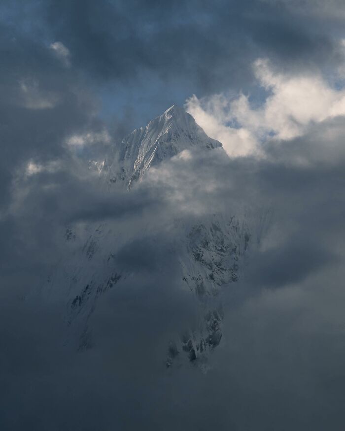 Snow-covered mountain peak emerging through dramatic clouds in breathtaking landscape photography resembling a fantasy movie scene.