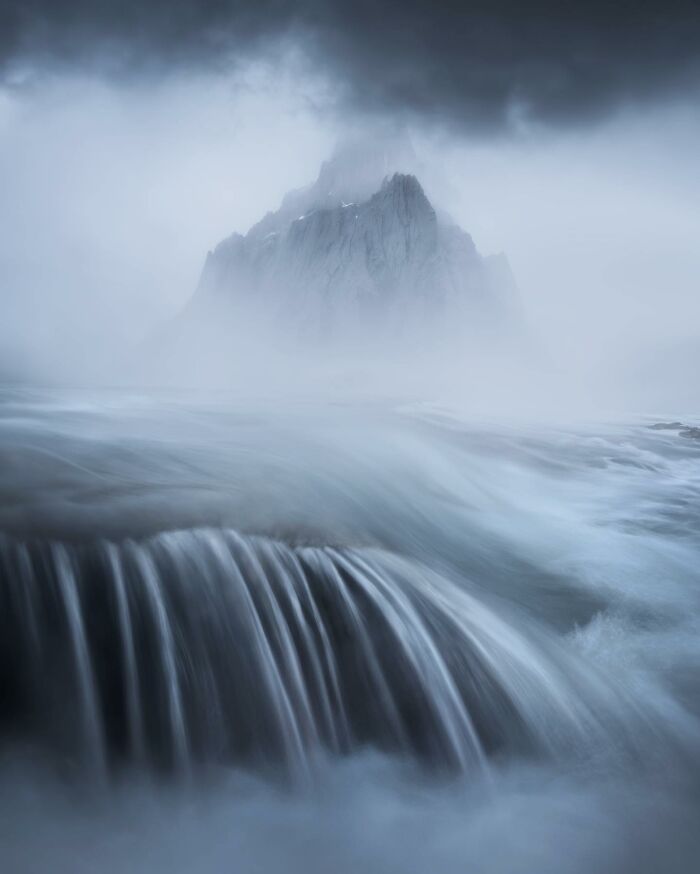 Mysterious landscape with flowing waterfall and jagged mountain shrouded in mist, capturing breathtaking fantasy-like scenery.