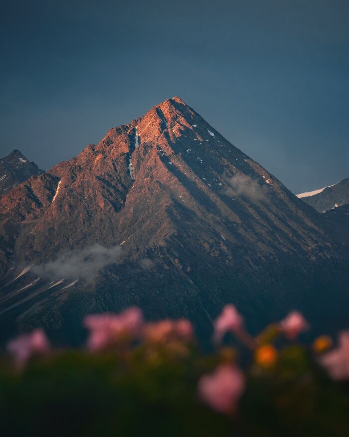 Sunlit mountain peak in a breathtaking landscape shot that looks straight out of a fantasy movie with blurred flowers in foreground.