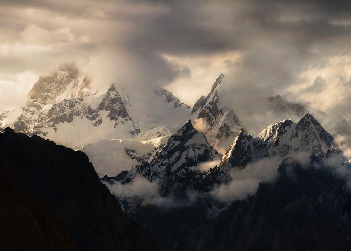 Snow-covered mountain peaks with clouds and dramatic lighting in breathtaking landscape photography scene.