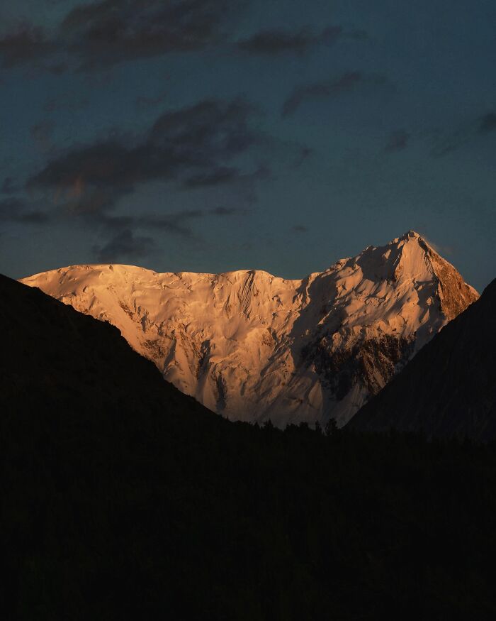 Snow-capped mountain landscape at sunset with dark foreground and dramatic sky, a breathtaking fantasy movie-like scene.