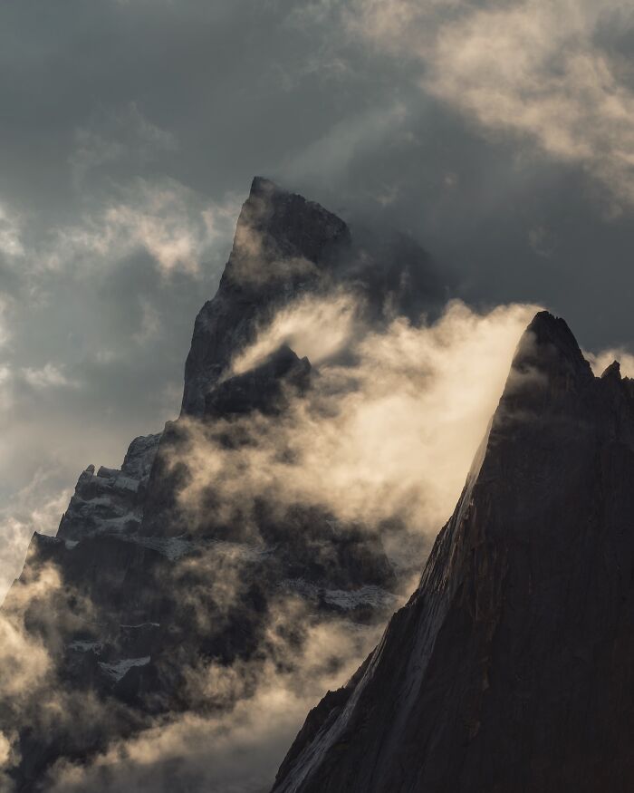 Dramatic landscape shot of jagged mountain peaks surrounded by swirling mist and clouds, creating a fantasy-like scene.