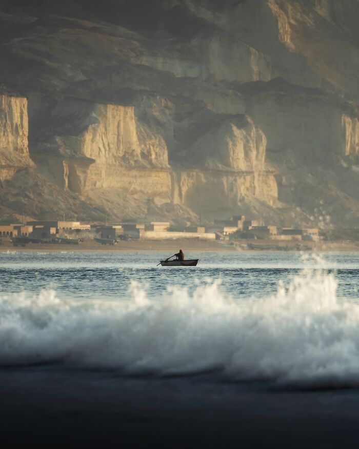 Breathtaking landscape shot of a lone boat on calm water with dramatic cliffs in the background, resembling a fantasy scene.