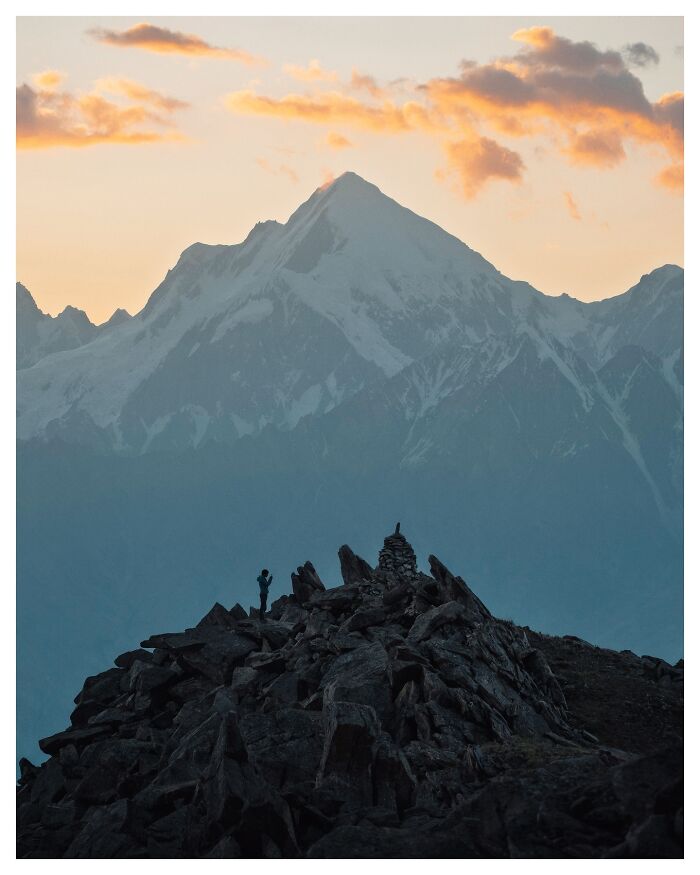 Photographer capturing breathtaking landscape shots of a mountain peak at sunset with dramatic clouds and rocky foreground.
