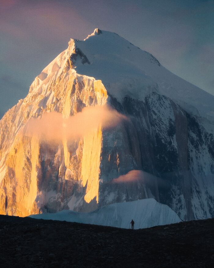 Breathtaking landscape shot of a towering snow-covered mountain with golden sunlight and soft clouds at dusk.