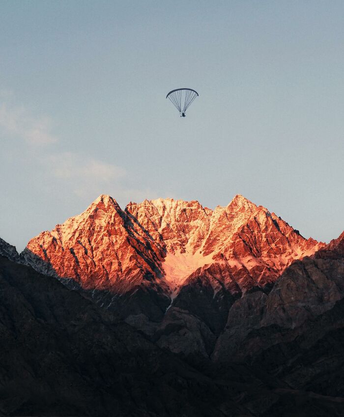 Paraglider flying above rugged mountain peaks at sunset, showcasing breathtaking landscape shots with fantasy movie vibes.