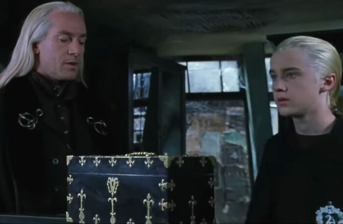 Two Harry Potter stars in character with long blonde hair, sharing a tense moment in a dark, magical setting.