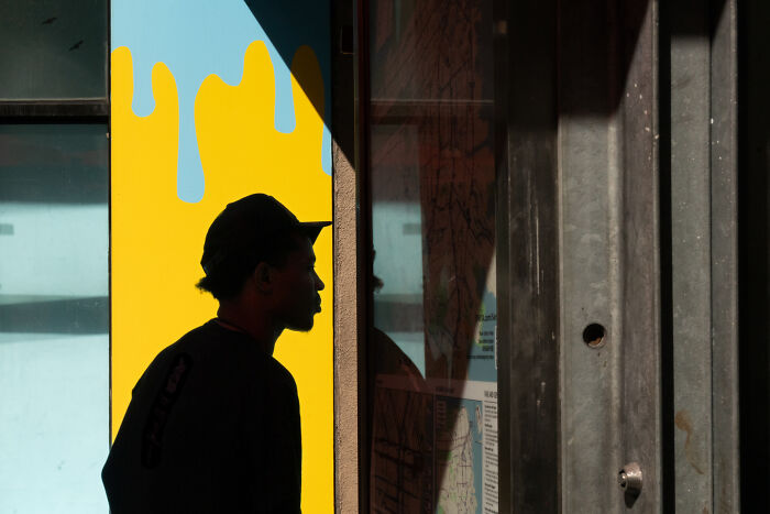 Silhouette of a man wearing a cap looking at a public map, captured in a candid moment by photographer snapping coincidental moments.
