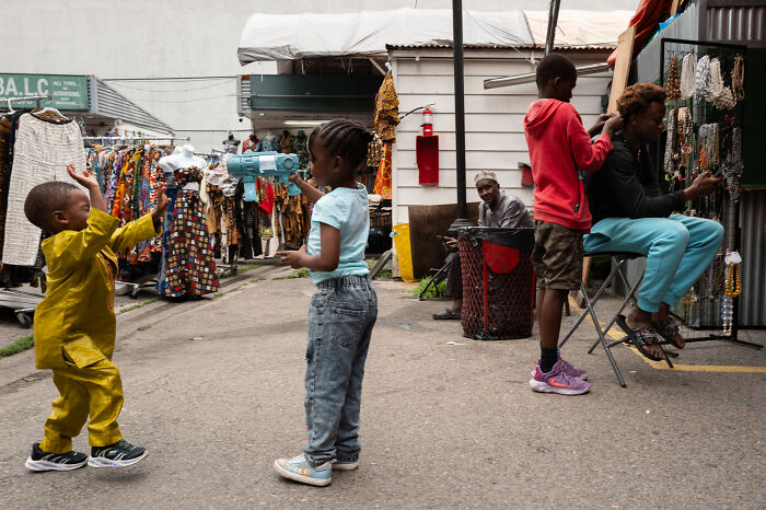 Children playing and interacting in a busy outdoor market, capturing a coincidental moment in public photography.