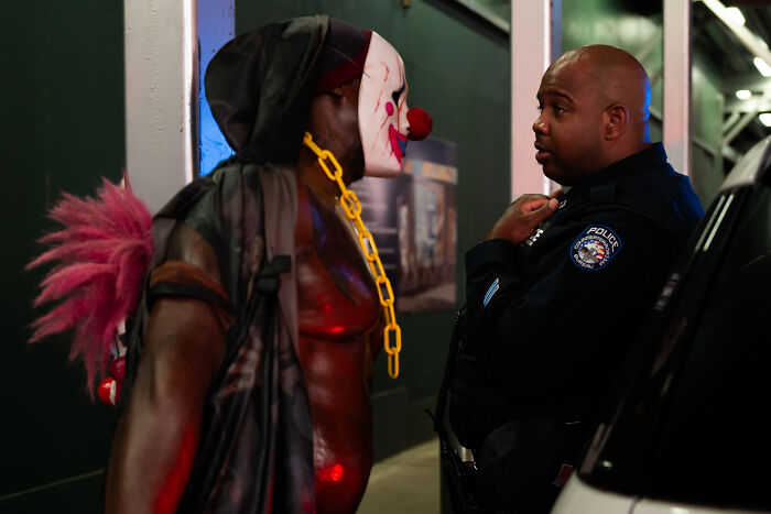 Man wearing clown mask and costume facing police officer in parking garage, a coincidental moment snapped in public.