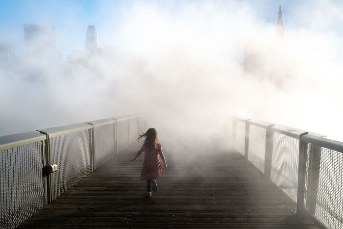 Child walking on foggy pier captured in a photographer snaps coincidental moments in public photograph.