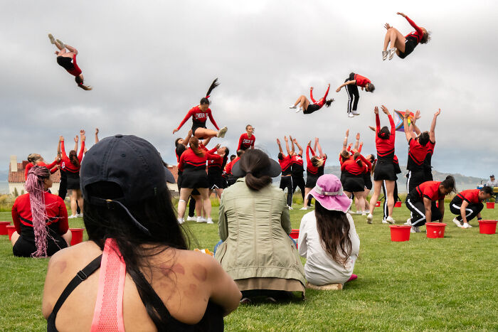 Cheerleaders captured in coincidental moments mid-air during a public outdoor performance with spectators watching.