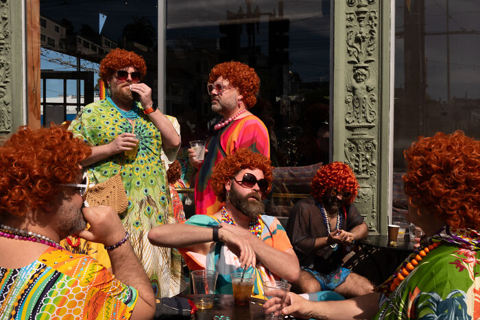 Group of men dressed in colorful clothes and red wigs captured in a public coincidental moment by a photographer.