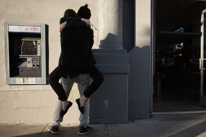 Couple captured in a coincidental public moment with one person giving the other a piggyback near an ATM machine.