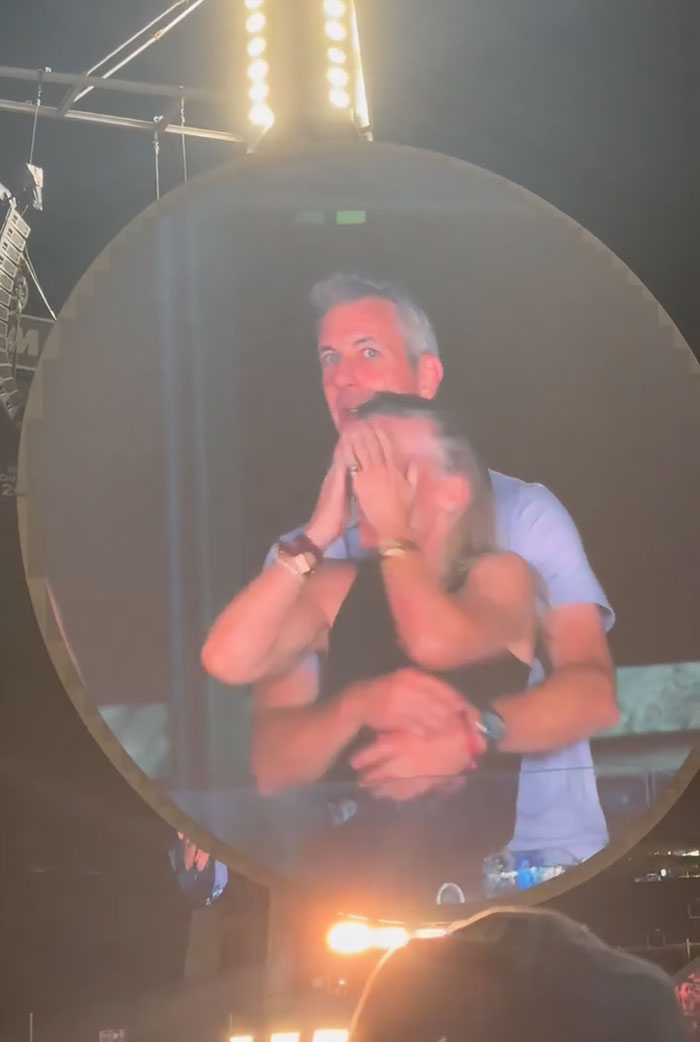 Man hugging woman on stage with a large circular screen in the background amid Coldplay scandal and CEO controversy.