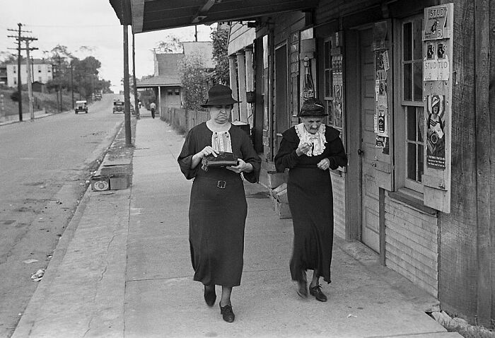 Two women walking on a sidewalk in a small town captured in rare photos from the Great Depression era.