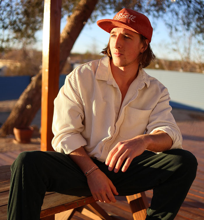Young man wearing a red cap and casual clothes sitting outdoors in warm sunlight, reflecting a relaxed mood.
