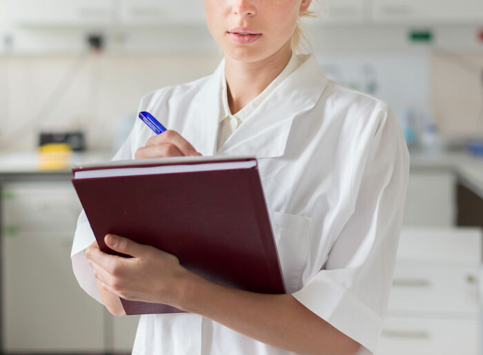 Female forensic scientist wearing white coat holding a file and pen, uncovering weird things while dealing with dead bodies
