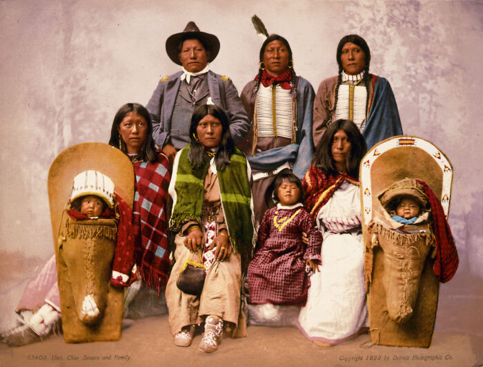 Vintage Native American family portrait with adults and children dressed in traditional clothing and cradleboards.