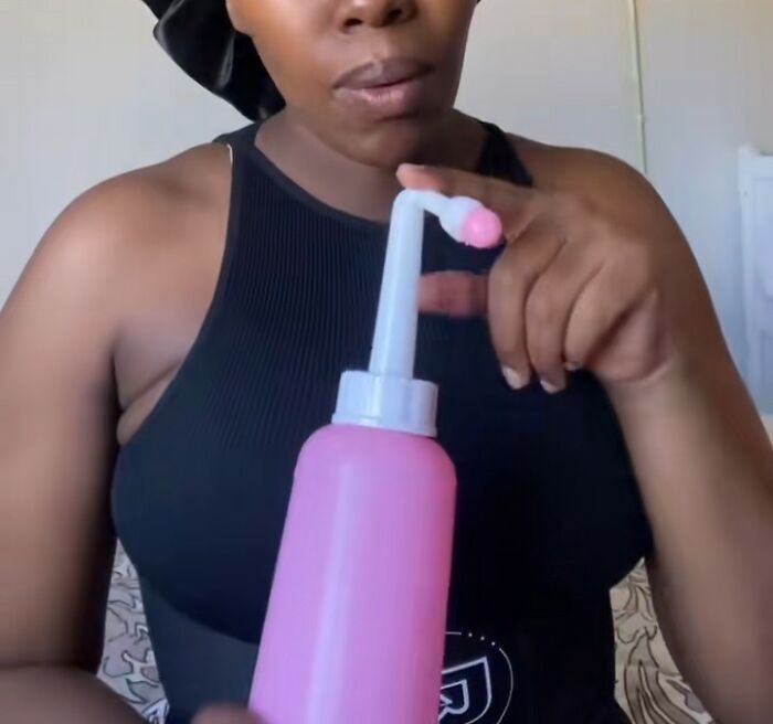 Woman in a black tank top holding a pink birth care bottle, illustrating challenges women face after birth.