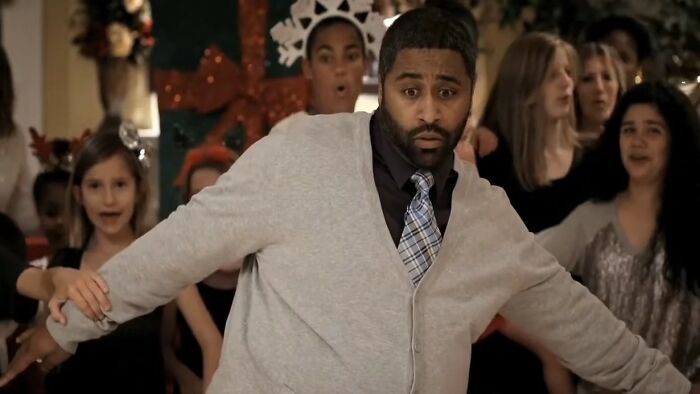 Man in a gray cardigan with a surprised expression dancing awkwardly among a crowd, illustrating worst movies of all time.