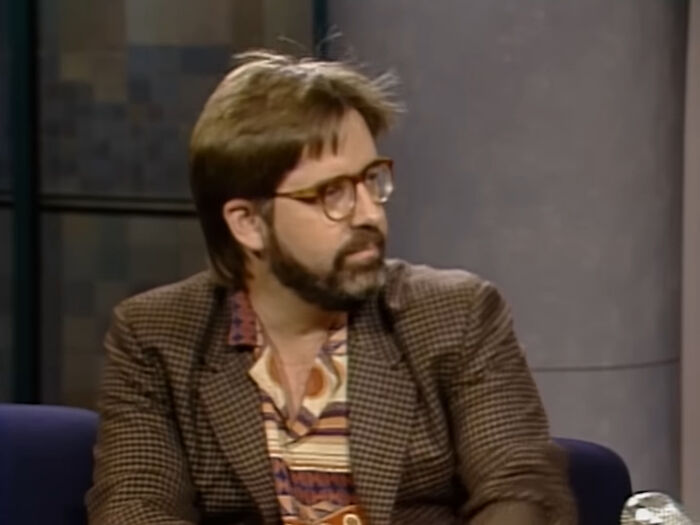 Man with glasses and beard in a brown checkered jacket, discussing Singapore experienced mass panic over shrinking genitals.