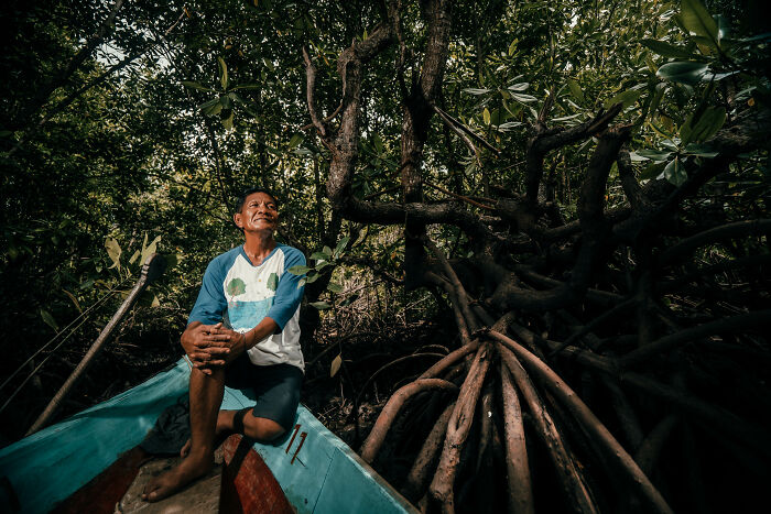 Man sitting on a boat surrounded by mangrove roots in a dense forest, capturing the spirit of mangrove photography awards.