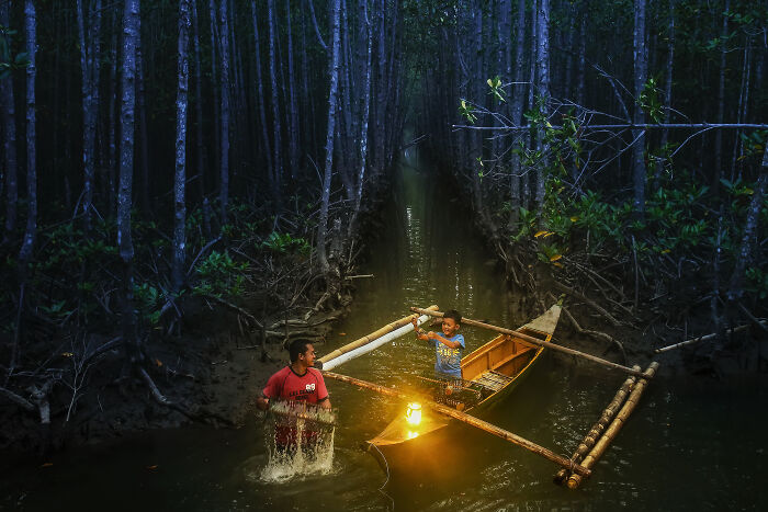 Two boys playing in a bamboo boat and shallow water surrounded by dense mangrove trees in a spectacular mangrove photography scene.