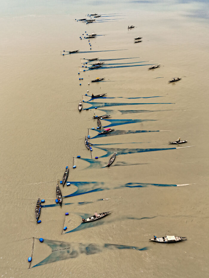 Aerial view of fishing boats and nets creating blue patterns in muddy waters for mangrove photography awards.
