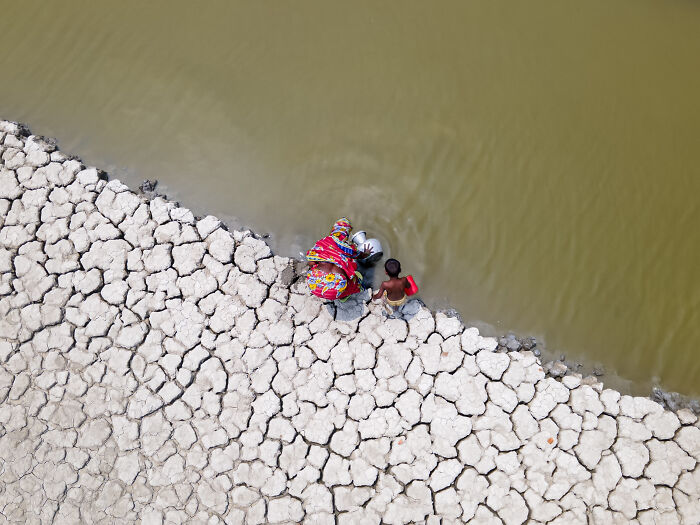 Aerial view of a woman and child collecting water near c*****d earth, highlighting environmental themes in mangrove photography awards.