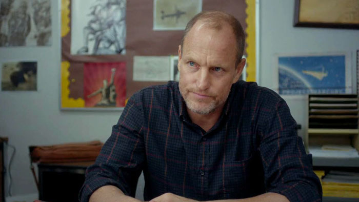 Man in a plaid shirt sitting at desk with framed artwork in background, related to Woody Harrelson fans stunned news. Man in a plaid shirt sitting at desk with framed artwork in background, related to Woody Harrelson fans stunned news.