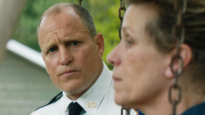 Woody Harrelson looking serious in a police uniform, with a woman blurred in the foreground, revealing his family background. Woody Harrelson looking serious in a police uniform, with a woman blurred in the foreground, revealing his family background.