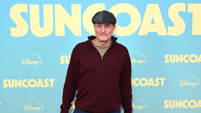 Woody Harrelson posing at a Disney+ Suncoast event, wearing a maroon sweater and a flat cap. Woody Harrelson posing at a Disney+ Suncoast event, wearing a maroon sweater and a flat cap.