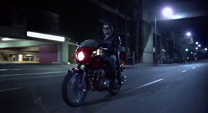 Man wearing sunglasses riding a motorcycle at night on an empty urban street for worst movie tropes quiz.
