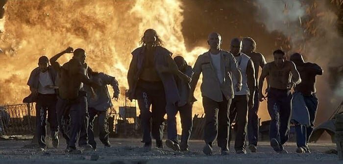 Group of men walking confidently away from a large fire explosion, illustrating a classic worst movie tropes scene.
