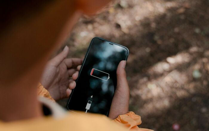Person holding a smartphone showing a low battery icon, illustrating frustration with common worst movie tropes quiz scenarios.