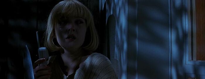 A woman in a dimly lit room holding a phone, evoking suspense typical of worst movie tropes quiz scenes.